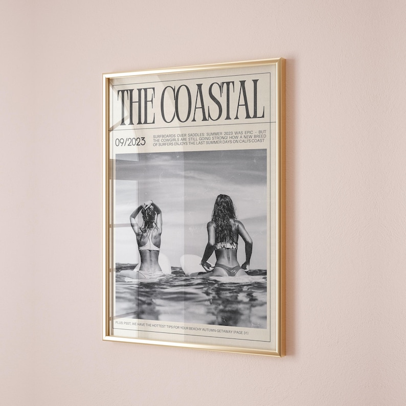 May include: A framed print with a gold frame. The black and white image shows two people in swimwear on surfboards in the sea. The text "THE COASTAL" is at the top, with "09/2023" below it.