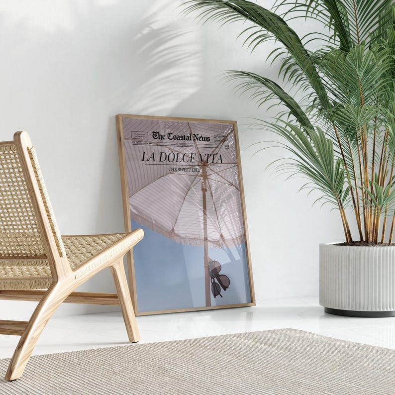 May include: A framed print of a newspaper article with the headline "La Dolce Vita" and a photo of a beach umbrella and sunglasses. The article is from "The Coastal News" and the date is "The Summer 2023".