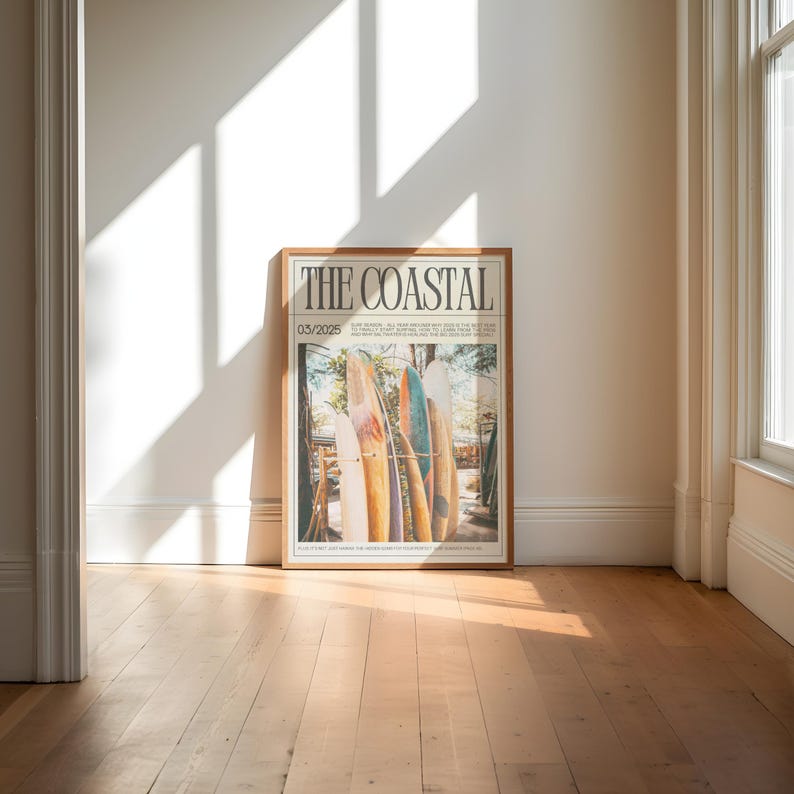 May include: A framed poster titled "THE COASTAL" featuring a photograph of several surfboards leaning against a wooden structure. The poster has a light brown wooden frame and is leaning against a white wall. The date "03/2025" is printed on the poster.