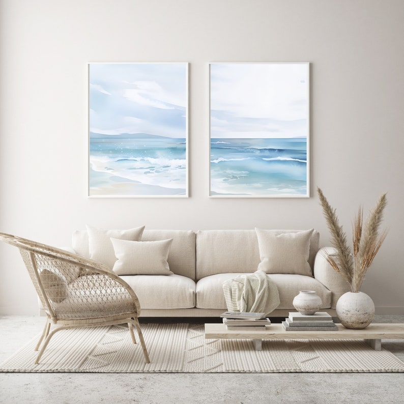 May include: Two framed watercolor paintings of a seascape with blue water and white waves. The paintings are hanging on a white wall above a beige sofa and a wicker chair.