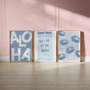 May include: Three framed prints with a blue background. The left print says "ALOHA" in white letters. The middle print is a guest check with the text "Meet me at the beach" and a heart symbol. The right print has a blue sky background with multiple blue lips printed on it.
