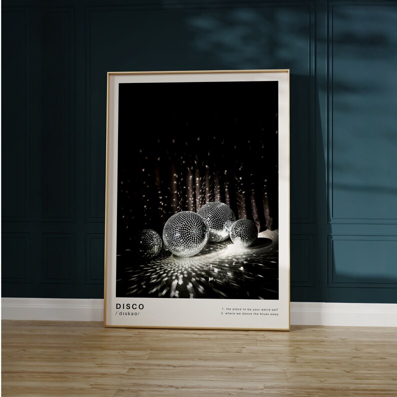 May include: A black and white poster with the word "DISCO" in bold white letters and the phonetic spelling "/ˈdɪskoʊ/" in smaller white letters. The poster features a photograph of five silver disco balls in a dark room with a black curtain in the background. The disco balls are reflecting light and casting shadows on the floor.