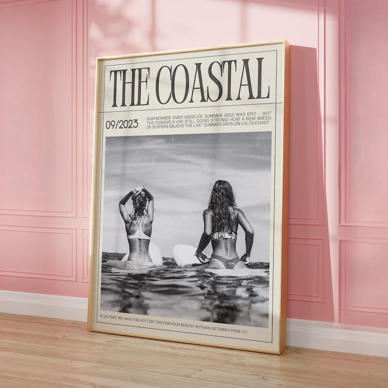 May include: A framed black and white print titled "THE COASTAL." The image shows two people on surfboards in the sea. The print has a beige frame and is against a pink wall. Text includes "09/2023" and article snippets.