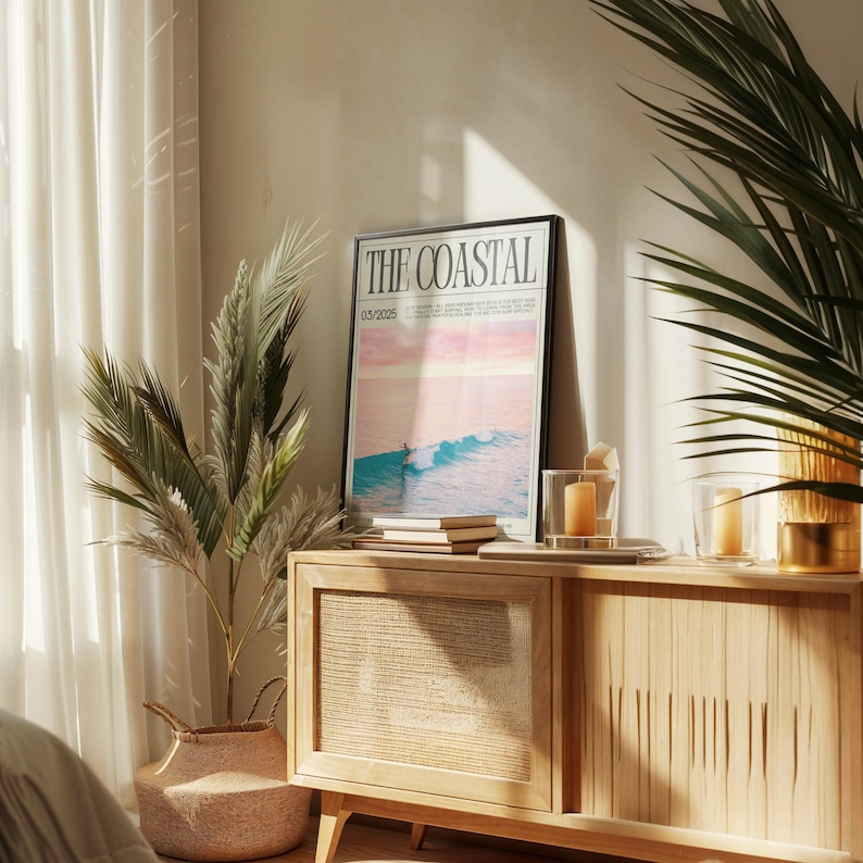 May include: A framed poster with the text "THE COASTAL" and a coastal scene, resting on a light wood cabinet. The cabinet has a woven panel and is decorated with candles and books. A potted plant and a basket are also in the image.