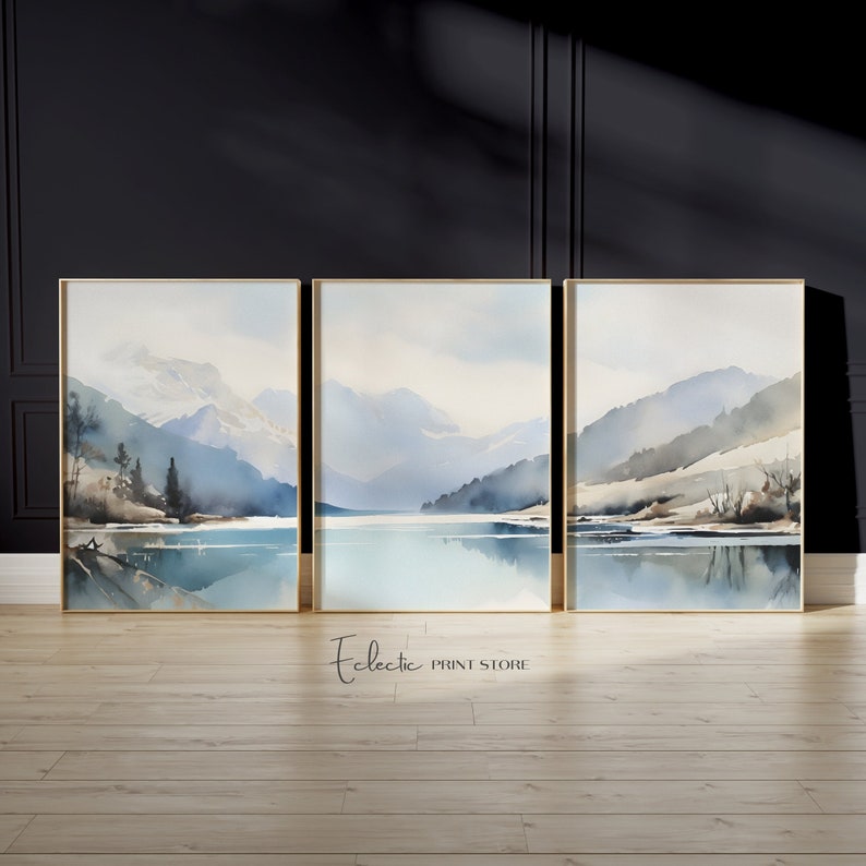 May include: A set of three watercolor paintings depicting a mountain lake scene. The paintings are framed in gold and feature a blue and white color scheme.