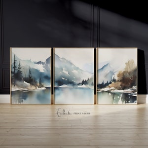 Könnte beinhalten: Drei gerahmte Aquarellbilder, die eine Bergseenlandschaft mit blauen und grünen Farbtönen darstellen. Die Bilder sind in goldenen Rahmen gefasst und in einer Reihe auf einem hellen Holzboden angeordnet.