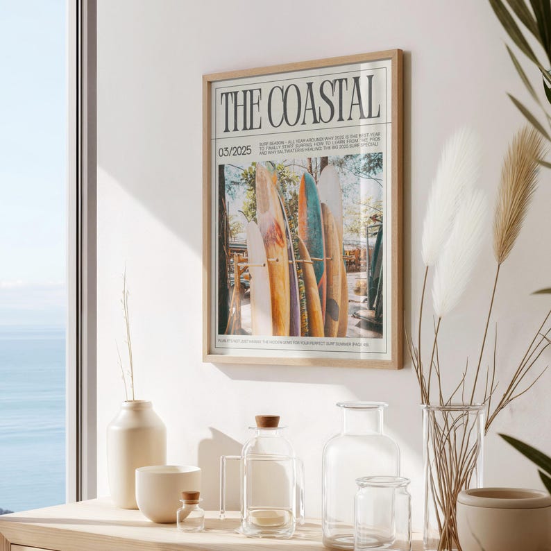 May include: A framed print titled "THE COASTAL" with a photograph of surfboards. The print is in a light wood frame and hangs on a white wall. The image includes the date 03/2025. The scene is near a window with a view of the ocean.