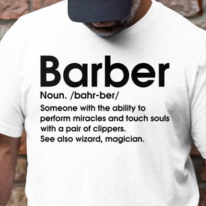 Puede incluir: Camiseta blanca con texto negro que dice "Barber" y una definición de la palabra. La definición dice: "Sustantivo. /bahr-ber/ Alguien con la capacidad de realizar milagros y tocar almas con un par de tijeras. Ver también mago, mago."