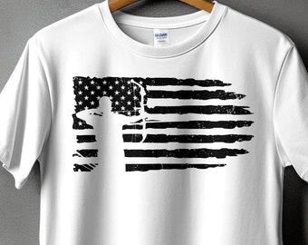 May include: White t-shirt featuring a distressed black and white graphic of the American flag with a silhouette of a person. The design is printed on a classic crew neck tee, perfect for casual wear.