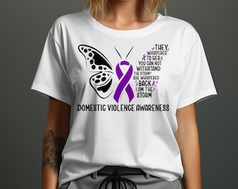 May include: White t-shirt with a purple ribbon and butterfly design. The text reads "They whispered to her& You can not withstand the storm She whispered back& I am the storm" and "Domestic Violence Awareness".