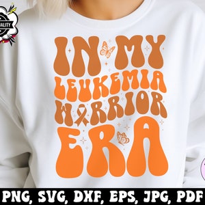 May include: White sweatshirt with an orange and brown graphic that says "In My Leukemia Warrior Era" with a butterfly and a ribbon.