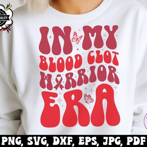 Op de afbeelding: Wit sweatshirt met een rood en roze grafisch ontwerp met de tekst "In My Blood Clot Warrior Era". De grafiek bevat een vlinder en een roze lint.