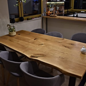 Könnte beinhalten: Ein großer, rustikaler Esstisch aus Holz mit einer natürlichen Holzmaserung. Der Tisch hat ein schwarzes Metallgestell und ist von sechs grauen Polsterstühlen umgeben.