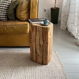 Könnte beinhalten: Ein rustikaler Beistelltisch aus einem Baumstamm mit einem Buch und einer blauen Tasse darauf. Der Tisch steht vor einem braunen Ledersofa mit Kissen und einem weißen Teppich.