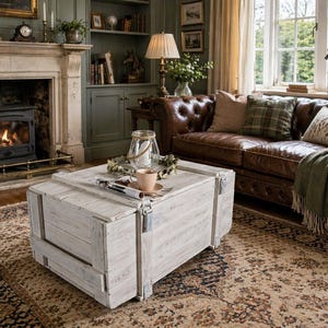 Könnte beinhalten: Ein rustikales Wohnzimmer mit einer weißen Holzkiste als Couchtisch. Ein braunes Ledersofa mit karierten Kissen und einer grünen Decke ist zu sehen. Ein Kamin mit Feuer und ein gemusterter Teppich vervollständigen die gemütliche Szene.