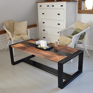 Op de afbeelding: Een rechthoekige salontafel met een donker gebeitst houten blad en een zwart metalen frame. De tafel heeft een modern design en staat in een woonkamer. De tafel is ongeveer 122 cm lang en 61 cm breed.