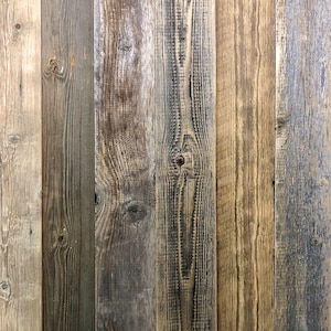 May include: A collection of vertical wooden planks featuring a weathered texture with visible grain patterns, knots, and a color palette ranging from light beige and tan to dark gray and brown tones, creating a rustic, multi-tonal surface.