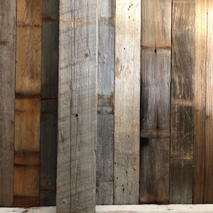May include: A collection of vertical wooden planks featuring varied textures and tones ranging from light gray to deep brown. The boards display natural grain patterns, visible knots, and weathered surfaces, arranged side-by-side in a panel.