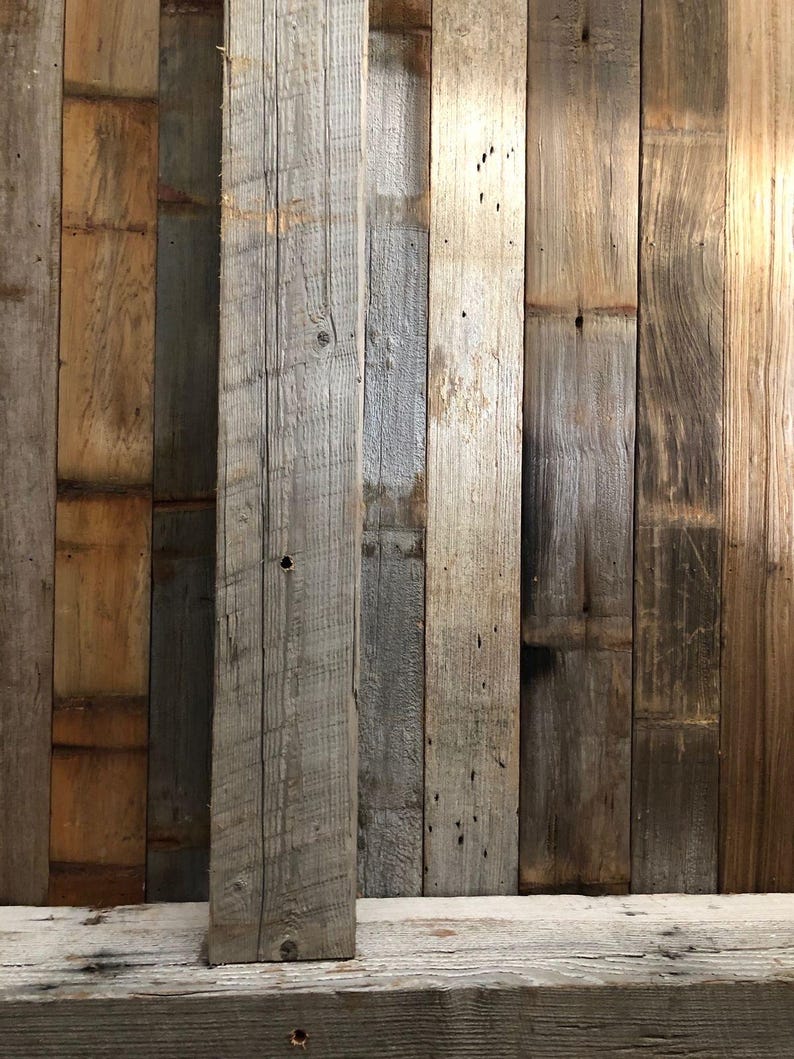 May include: A collection of vertical wooden planks featuring varied textures and tones ranging from light gray to deep brown. The boards display natural grain patterns, visible knots, and weathered surfaces, arranged side-by-side in a panel.