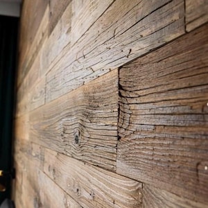 May include: A wall covered in horizontal wooden planks featuring a weathered brown texture with visible grain patterns, knots, and deep fissures. The planks are arranged in a staggered pattern, showcasing a rough, aged surface finish.