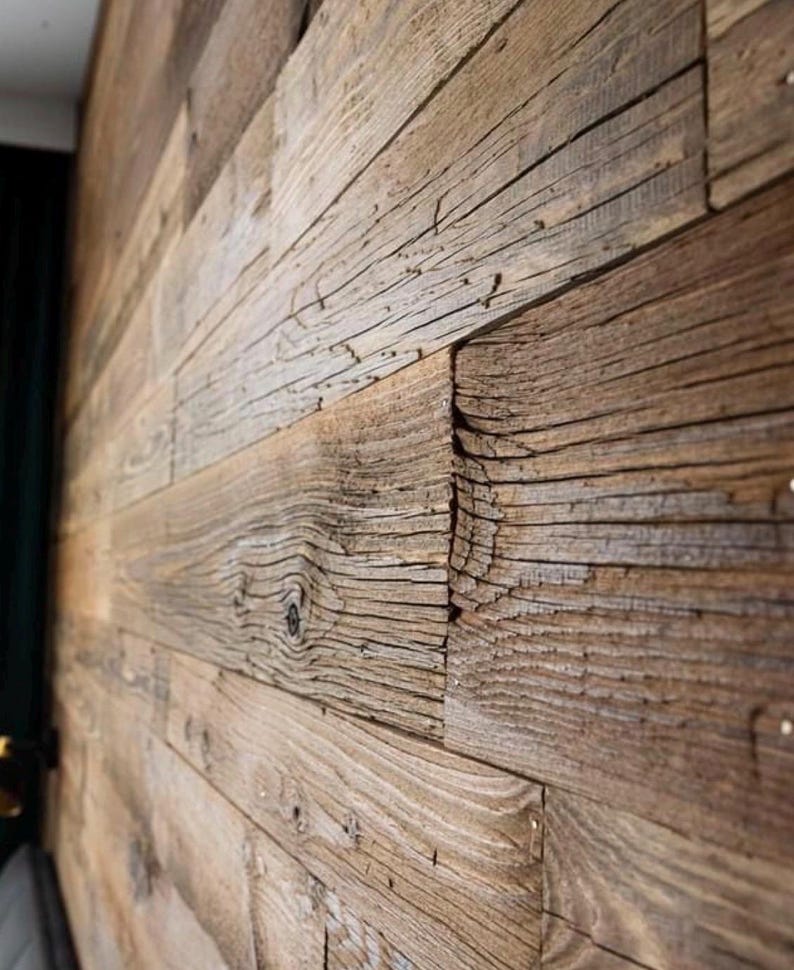 May include: A wall covered in horizontal wooden planks featuring a weathered brown texture with visible grain patterns, knots, and deep fissures. The planks are arranged in a staggered pattern, showcasing a rough, aged surface finish.
