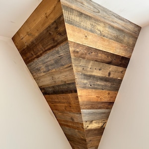 May include: A triangular corner shelf constructed from horizontal planks of reclaimed wood. The wood features a variety of natural brown and gray tones, showcasing visible grain patterns, knots, and weathered textures throughout the structure.