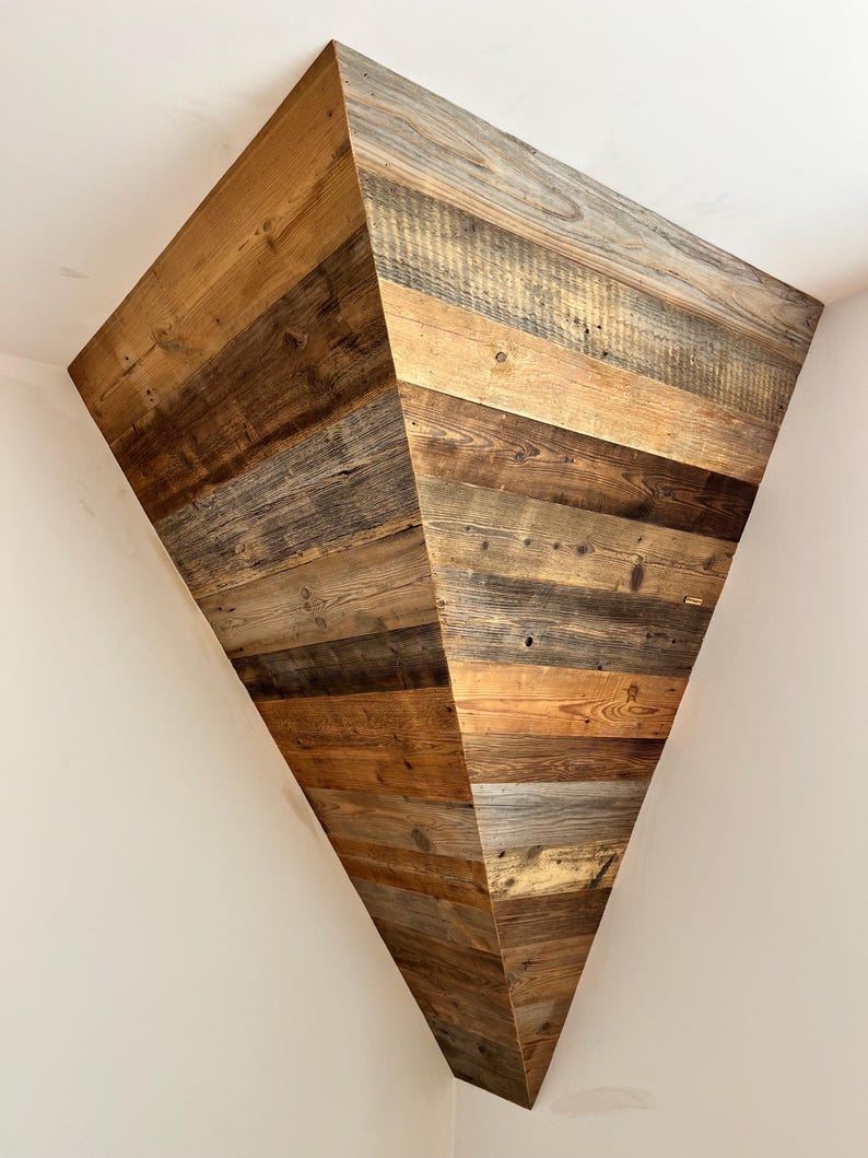 May include: A triangular corner shelf constructed from horizontal planks of reclaimed wood. The wood features a variety of natural brown and gray tones, showcasing visible grain patterns, knots, and weathered textures throughout the structure.