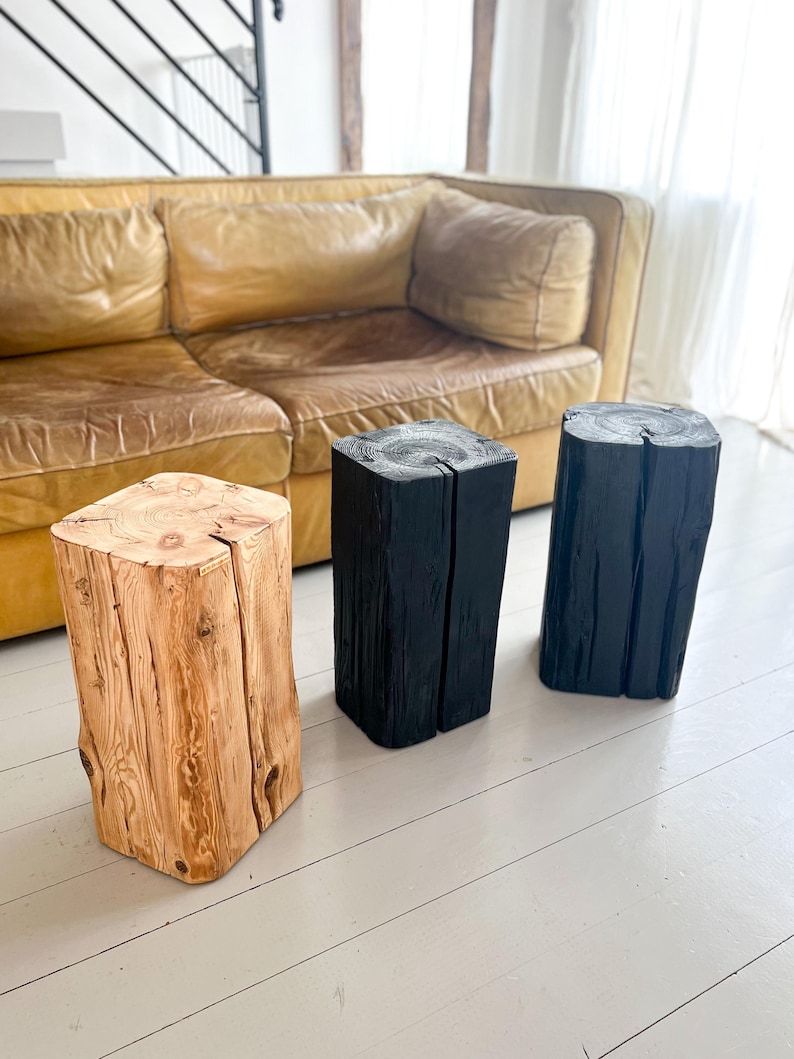 May include: Three vertical wooden stools with a square cross-section and a central vertical split. One stool features a natural light brown wood grain finish, while the other two stools are finished in a solid matte black color.