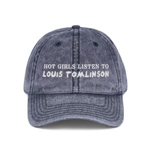 May include: A denim blue baseball cap with the text "HOT GIRLS LISTEN TO LOUIS TOMLINSON" embroidered in white. The cap has a curved brim and an adjustable strap at the back. The hat is a vintage style.