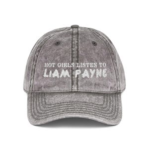 May include: Gray baseball cap with the text "HOT GIRLS LISTEN TO LIAM PAYNE" in white. The cap has a curved brim and an adjustable strap. The hat is made of a soft, worn material.