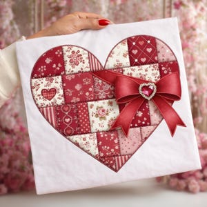 Könnte beinhalten: Ein herzförmiges Patchwork-Design in Rot- und Weißtönen, verziert mit einer großen roten Schleife und einem herzförmigen Schmuckstück. Der Patchwork-Stoff weist verschiedene florale und gemusterte Stoffe auf, die eine romantische und handwerkliche Ästhetik schaffen.