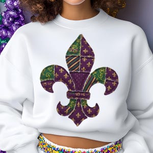 Könnte beinhalten: Weißes Sweatshirt mit einem großen, farbenfrohen Fleur-de-Lis-Design. Das Fleur-de-Lis besteht aus grünem, lila und goldfarbenem Stoff mit einem Patchwork-Effekt. Das Design befindet sich mittig auf der Vorderseite des Sweatshirts.