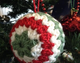 May include: A crocheted Christmas ornament in red, white, and green. The ornament is shaped like a ball and has a spiral pattern.