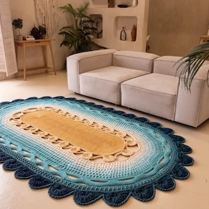 Peut inclure: Un tapis ovale fait à la main avec un bord festonné. Le tapis présente un dégradé de couleurs, passant d'une bordure bleu foncé au bleu clair, blanc et un centre beige. Le tapis est posé sur un sol de couleur claire dans un salon.