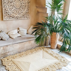 May include: A beige crocheted rug with a delicate lace border, placed on a light wood floor in a room with a white wall and a carved wooden panel.