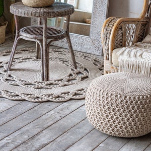 May include: A beige crocheted ottoman with a woven wicker chair and a round crocheted rug in a living room setting.