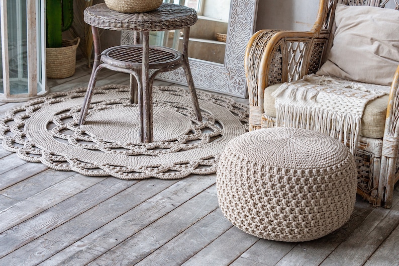 May include: A beige crocheted ottoman with a woven wicker chair and a round crocheted rug in a living room setting.