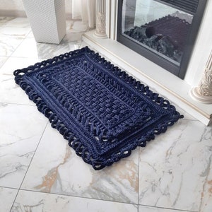 Può includere: Un tappeto all'uncinetto blu navy con un bordo decorativo. Il tappeto è realizzato con filato spesso e ha una superficie testurizzata.