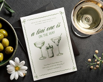 May include: A baby shower invitation with the text "a tini one is on the way" in green script. The invitation features illustrations of a martini glass, a baby bottle, and a cocktail glass. Olives, a flower, and a glass of liquid are also visible.