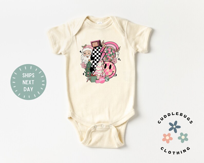 K&ouml;nnte beinhalten: Ein cremefarbener Baby-Strampler mit einem pinkfarbenen und gr&uuml;nen Weihnachtsmotiv. Das Motiv zeigt einen Weihnachtsmann, einen Weihnachtsbaum, einen Regenbogen, ein Karomuster und ein Smiley.