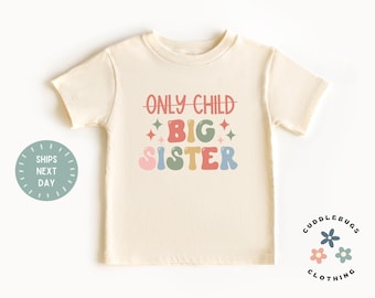 Può includere: T-shirt color crema per bambini con la scritta "ONLY CHILD BIG SISTER" in un font retrò colorato. Il design include stelle. La maglietta ha girocollo e maniche corte. Da Cuddlebugs Clothing.