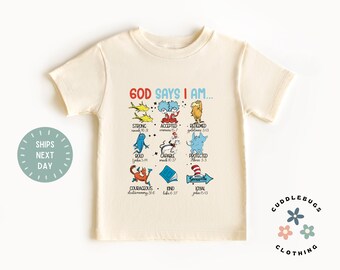 May include: A beige t-shirt with a graphic of various Dr. Seuss characters and the text "GOD SAYS I AM..." with bible verses listed below each character. The characters include Thing 1, Thing 2, the Cat in the Hat, and the Lorax.