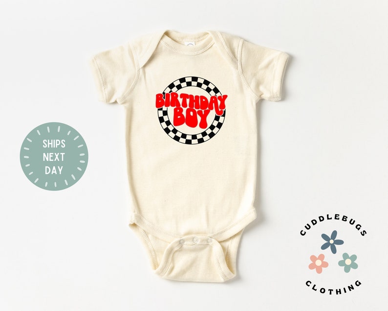 K&ouml;nnte beinhalten: Ein cremefarbener Baby-Strampler mit einem roten und schwarzen karierten Kreisdesign. Der Text "Birthday Boy" ist in roten Buchstaben innerhalb des Kreises geschrieben.