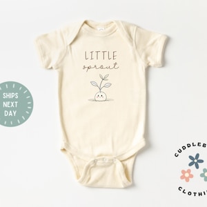 May include: Cream-colored baby bodysuit with the words "Little Sprout" and a small sprout illustration in black ink. The bodysuit has short sleeves and snap closures. The Cuddlebugs Clothing logo is in the bottom right corner.