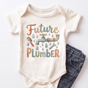 May include: A cream-colored short-sleeve baby bodysuit featuring a graphic print with the text Future Plumber in multi-colored letters. The design includes a central water faucet, a pipe, a wrench, and several small blue water droplets.