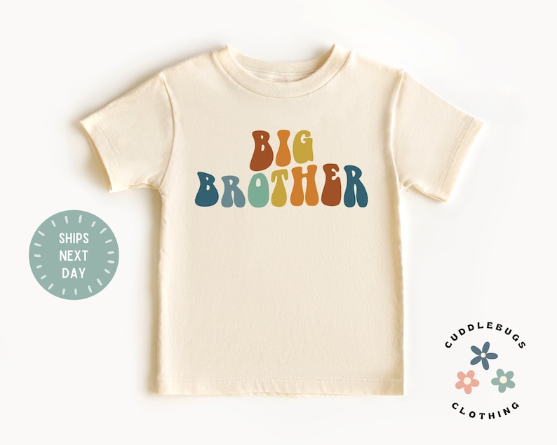May include: A cream colored t-shirt with the words "BIG BROTHER" in rainbow colored retro font.