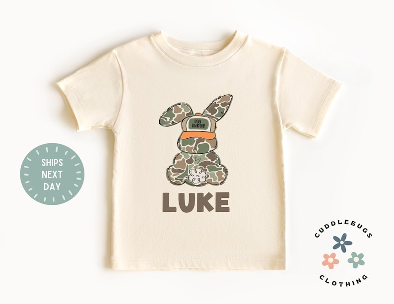 May include: A beige short-sleeved t-shirt with a camouflage bunny wearing a hat that says "Top Hunter" and the name "LUKE" printed below the bunny.