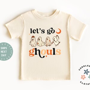 K&ouml;nnte beinhalten: Ein cremefarbenes T-Shirt mit einer Grafik von Geistern und dem Text "Let's go ghouls".