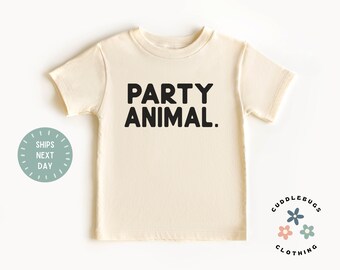 May include: A cream colored short-sleeved t-shirt with the text "PARTY ANIMAL." printed in black.