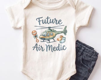 May include: An off-white short-sleeve baby bodysuit featuring a graphic of a green helicopter, a rattle, and two small socks. The text "Future Air Medic" is printed in blue above and below the helicopter illustration. Dark gray denim pants.